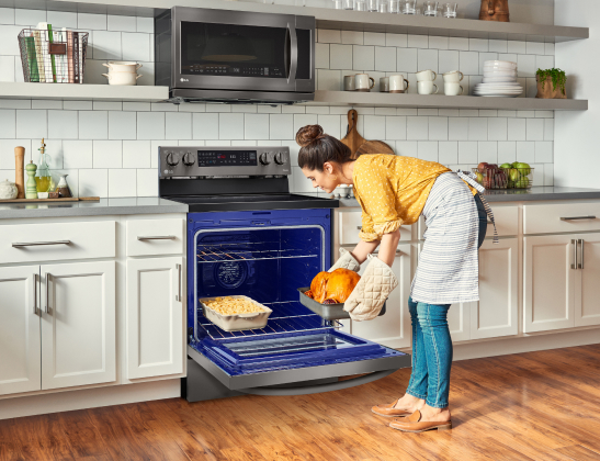 woman putting a roast chicken in the oven, featuring the blue inside of the oven